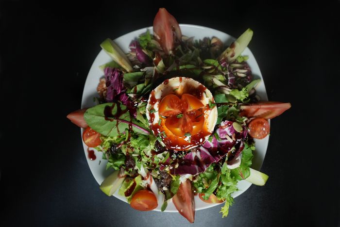 Ensalada de queso de cabra gratinado con hojas verdes, tomate cherry y reducción de balsámico