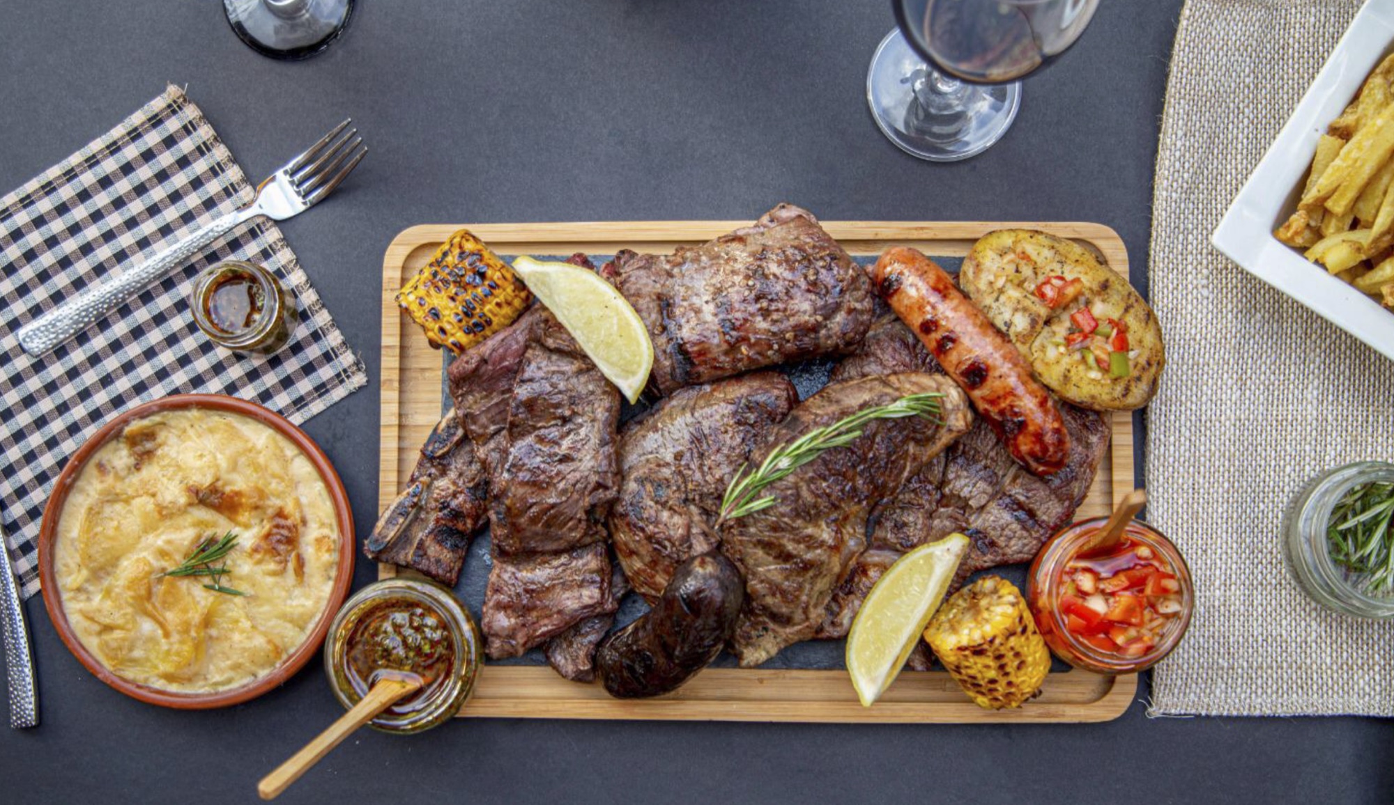 Parrillada argentina servida para compartir, con carnes, guarniciones y chimichurri