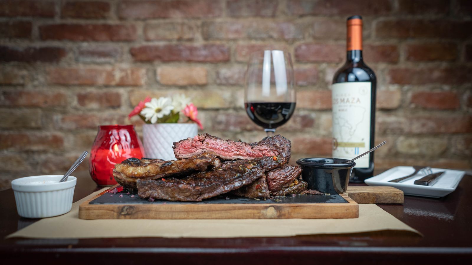Costillar y bife recién cortados, servidos junto a una copa de vino tinto sobre una mesa de madera